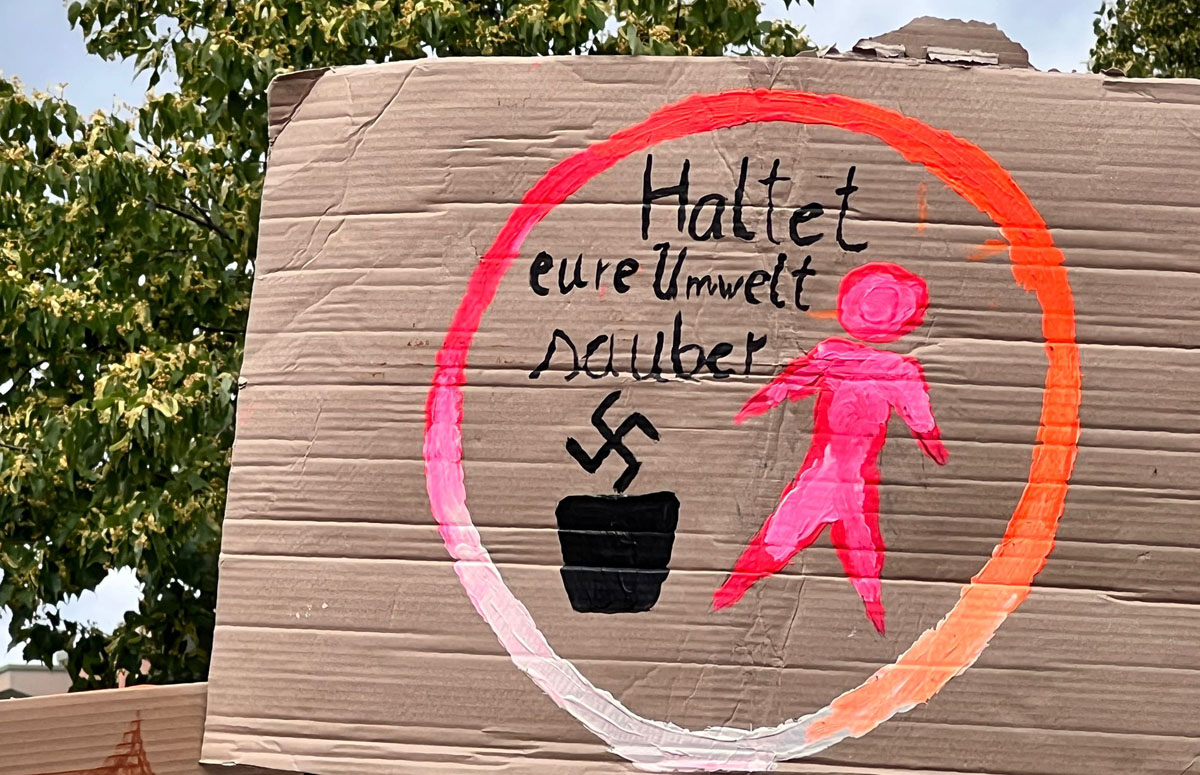 Selbstgemaltes Protestplakat gegen die AfD: Figur wirft ein Hakenkreuz in einen Mülleimer mit der Überschrift " Haltet eure Umwelt sauber!"